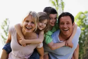 A family of four - a mother, father, and two children - smiling and embracing outdoors