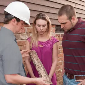 Three construction workers examining plans together near a brick building