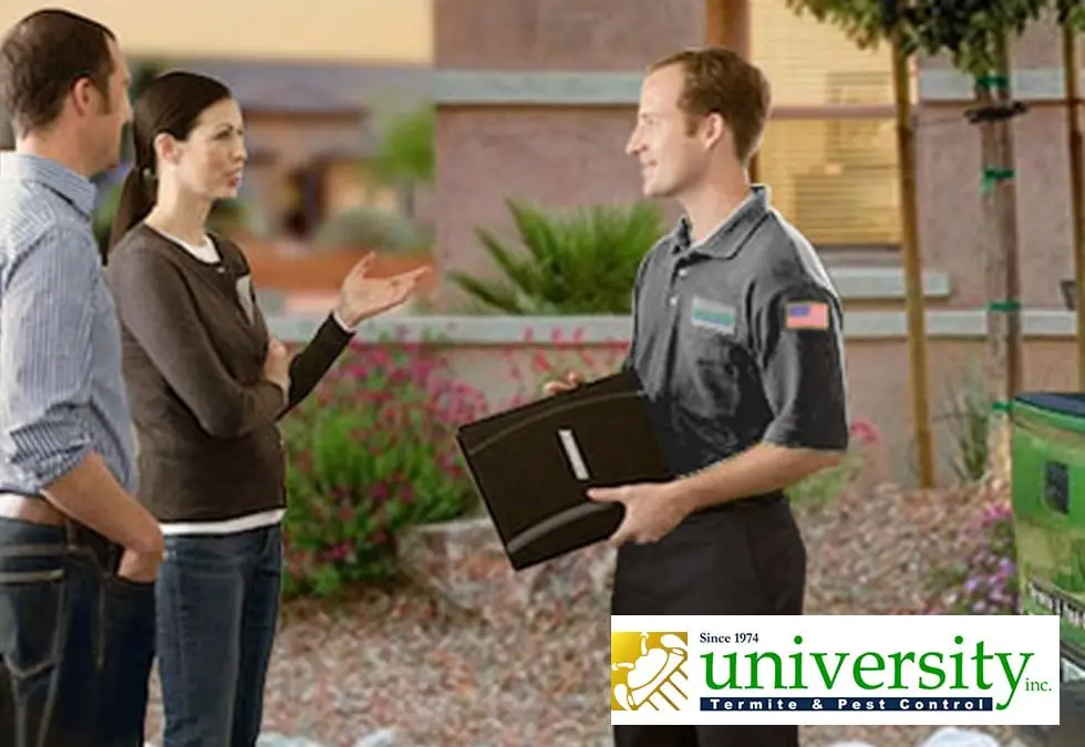 A pest control technician talks with two homeowners outdoors. Logo for University Termite & Pest Control is visible in the corner.