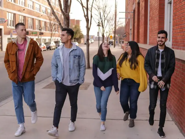 A group of five young people walking together on a city street, wearing casual clothing and smiling