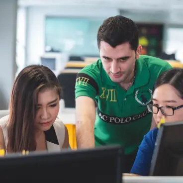 Three people, two women and one man, gathered around a computer screen and interacting