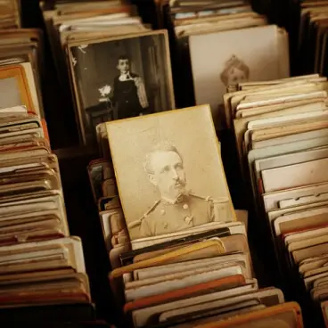A sepia-toned image showing various framed photographs and portraits stacked on top of each other, suggesting a collection or archive of historical images.
