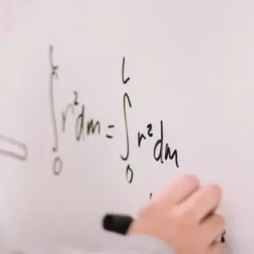 A person's hand writing mathematical equations or formulas on a whiteboard